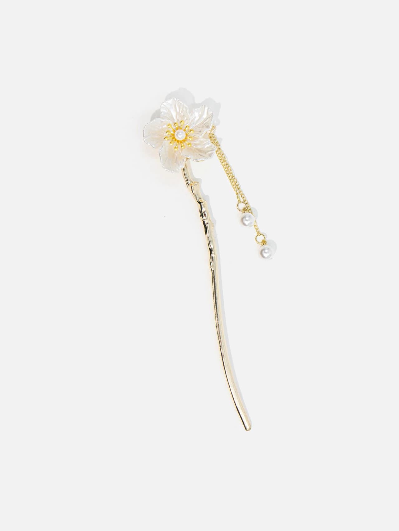 Guldfärgad hårnål med vit blomma, hängande kedja och två pärlor mot ljus bakgrund.