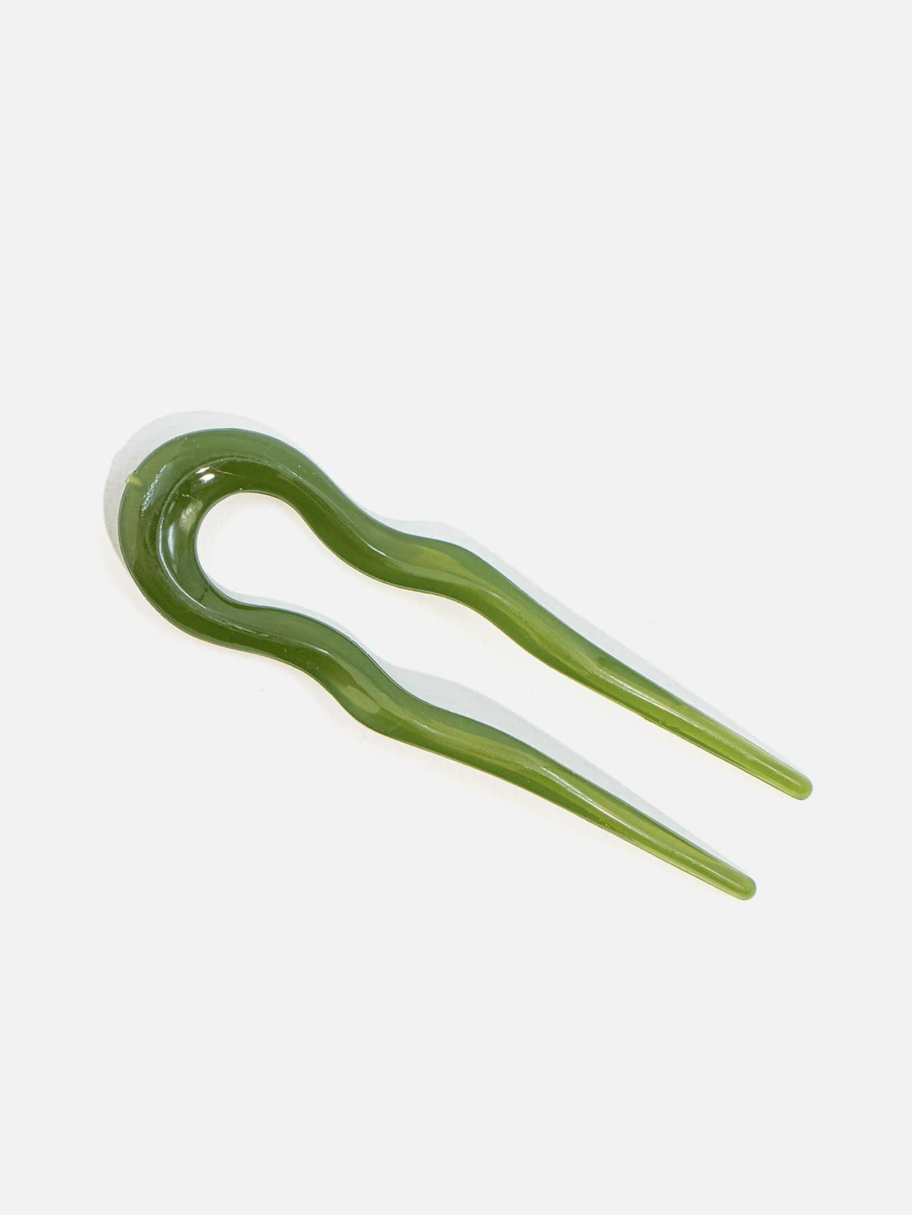 Grön U-formad hårpinne i plast med blank yta på vit bakgrund från top