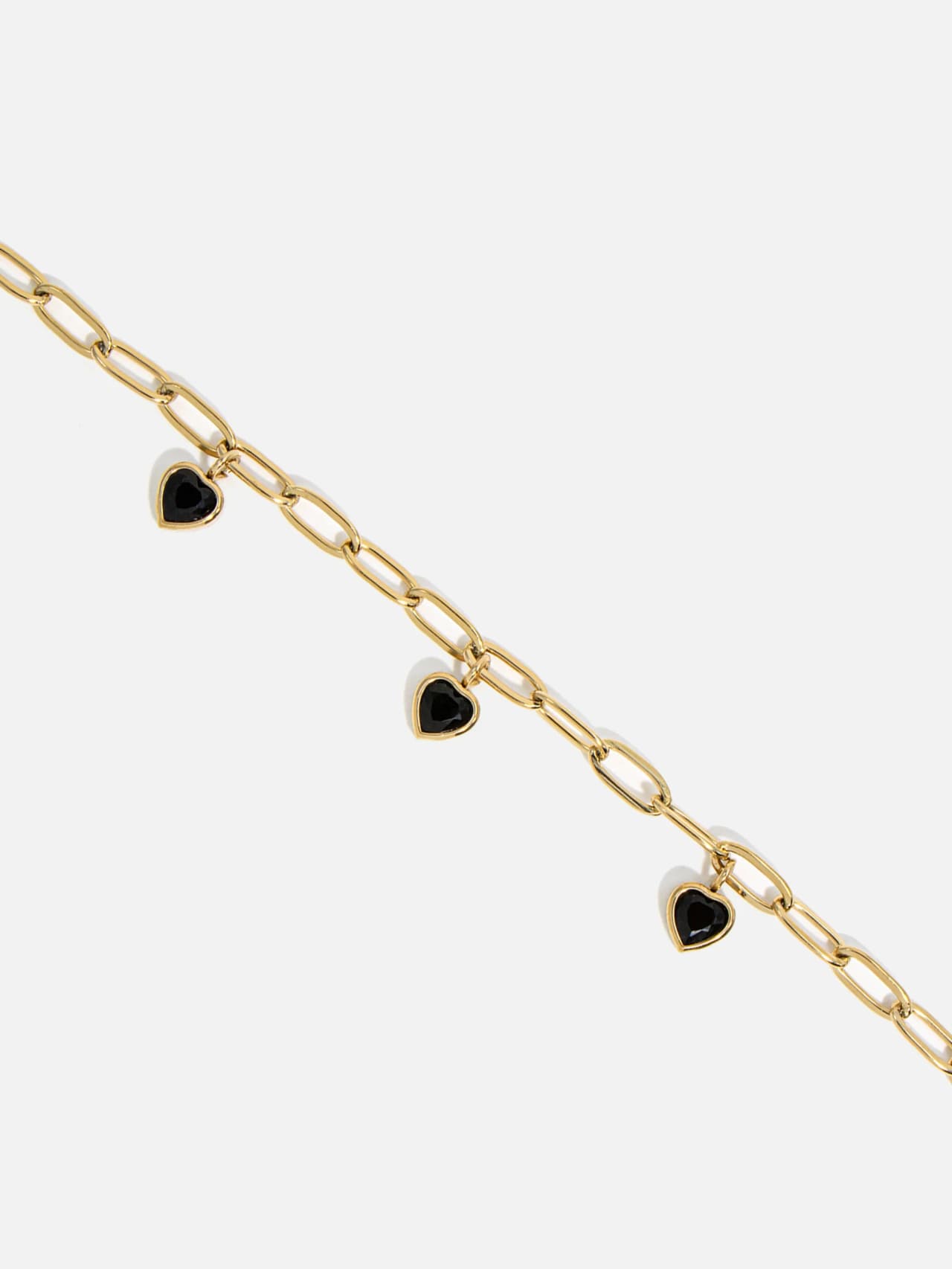 Närbild på svarta hjärtformade stenhängen på guldpläterat kedjearmband