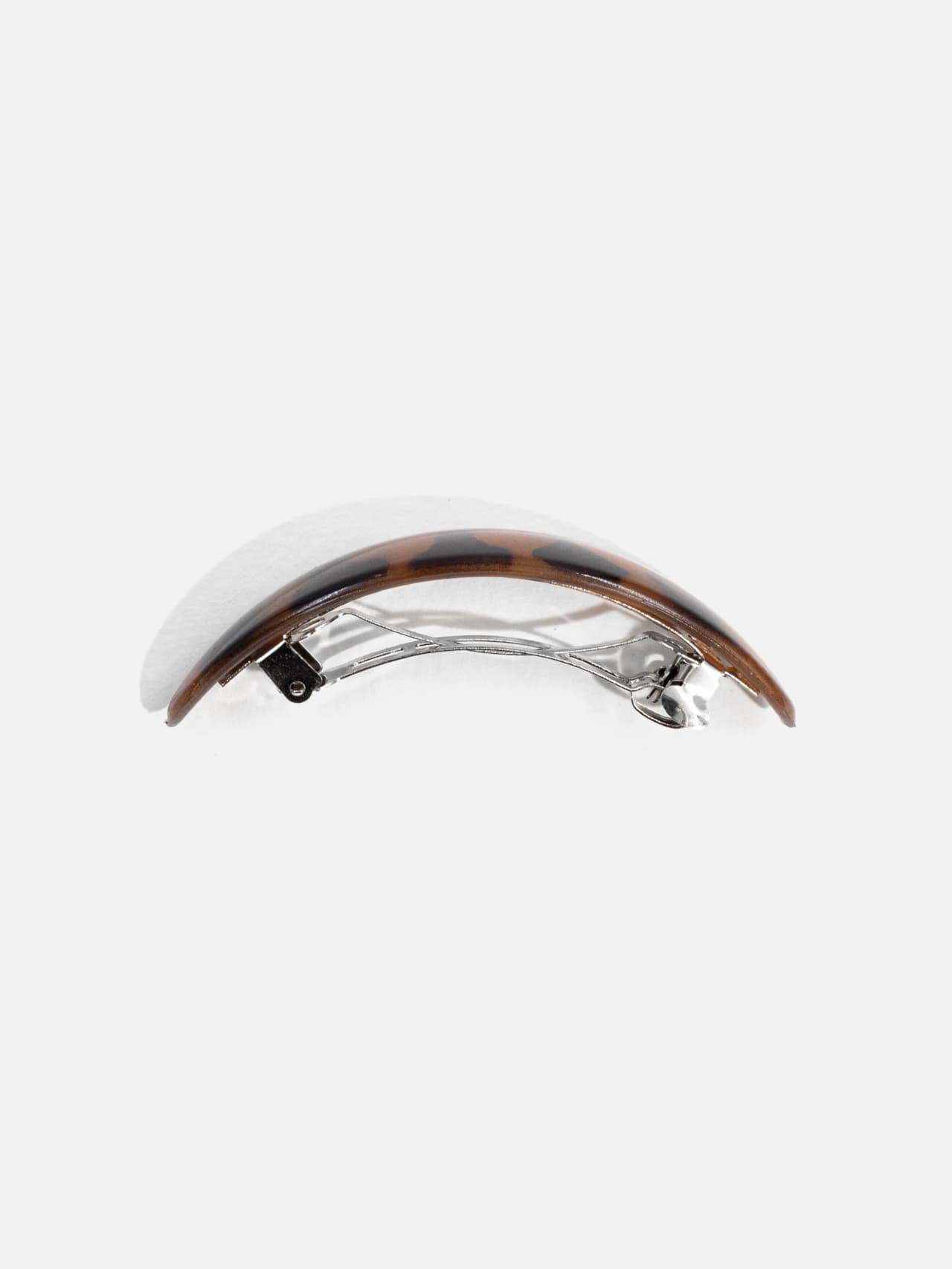 Hårspänne sett från sidan med bågformad profil och metallspänne undertill, ca 8 cm.