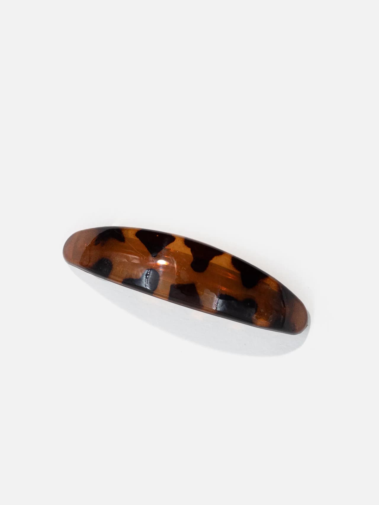 Bågformat hårspänne i amber-brunt sköldpaddsmönster på vit bakgrund, ca 8 cm.
