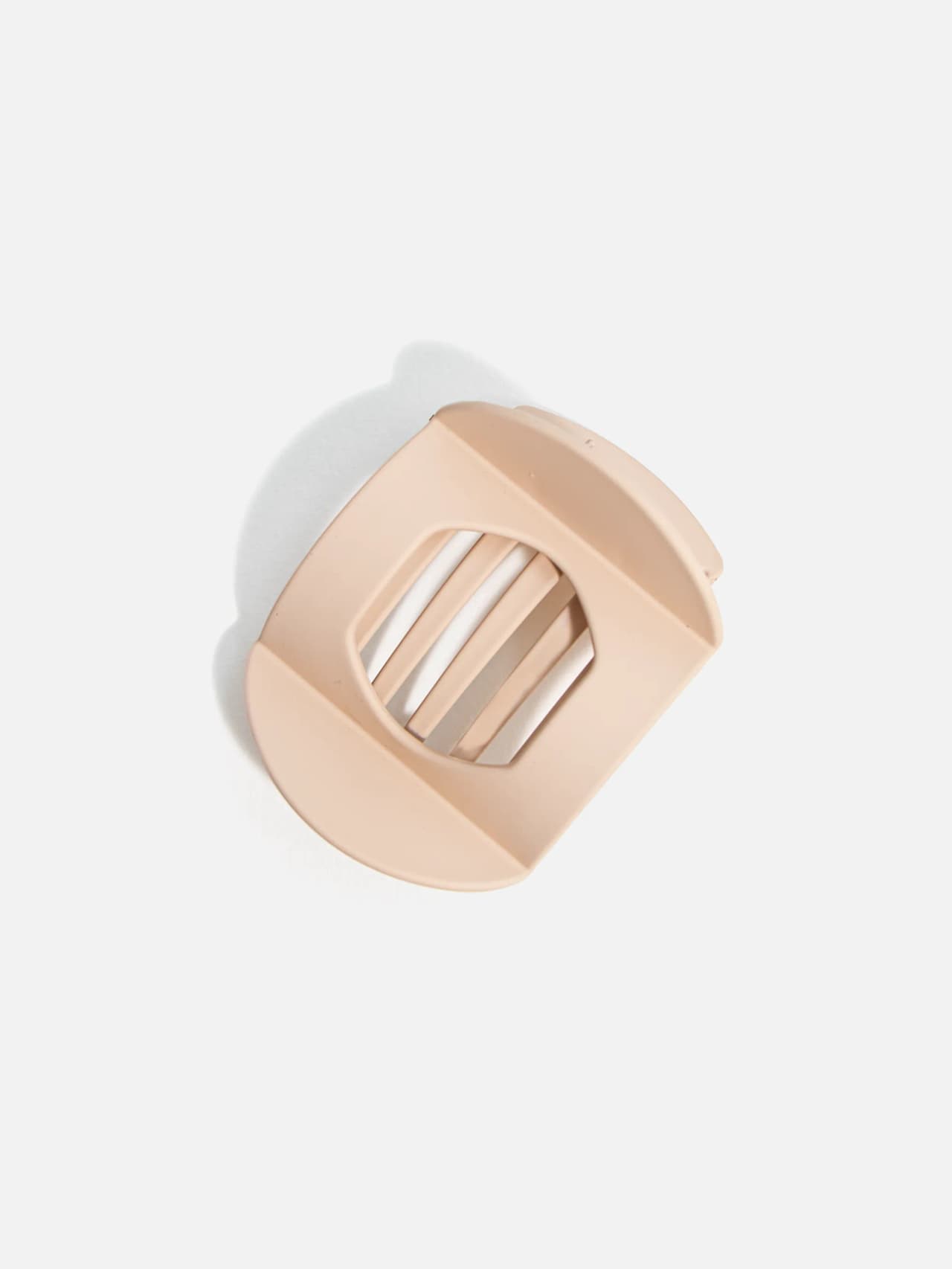 Oval hårklämma i beige ton med öppen ribbad form, sedd snett uppifrån