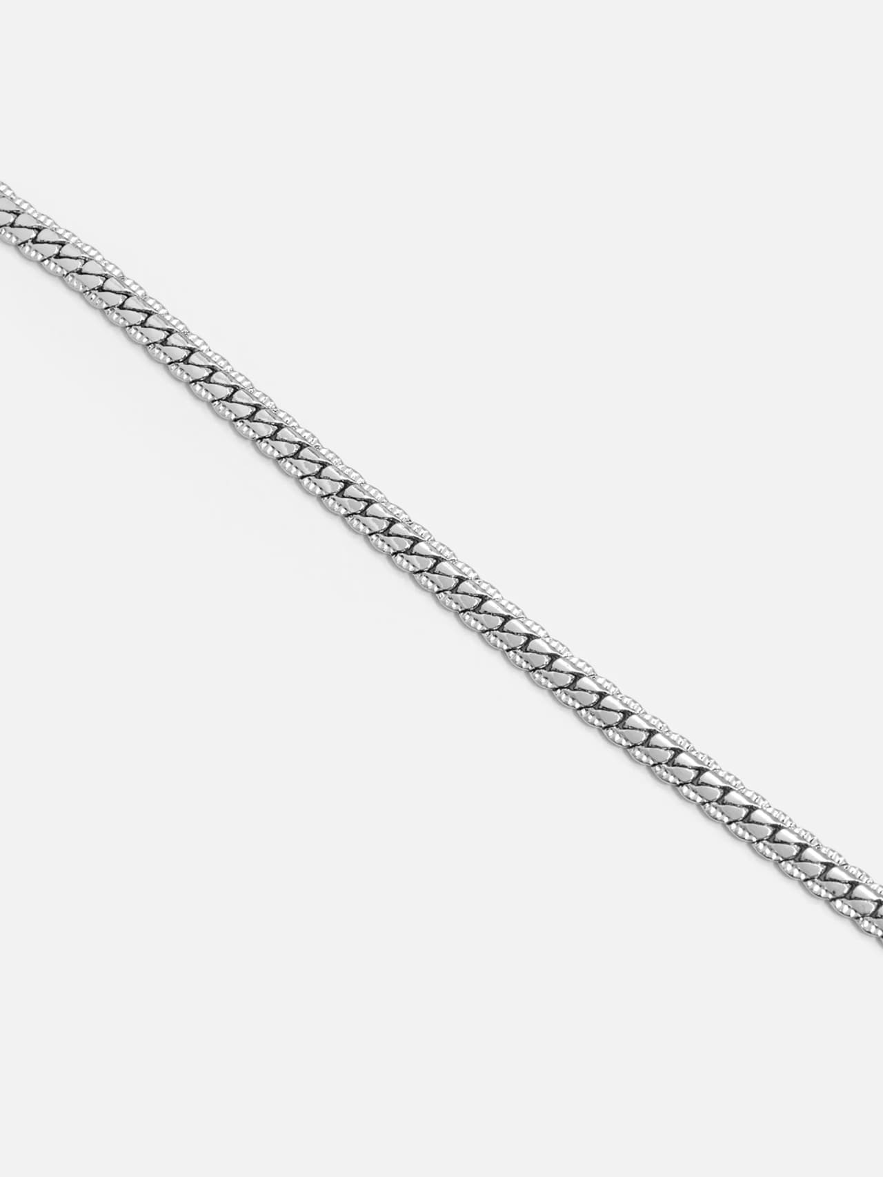 Närbild på platinapläterat armband med pressad pansarlänk och markerad kantstruktur.