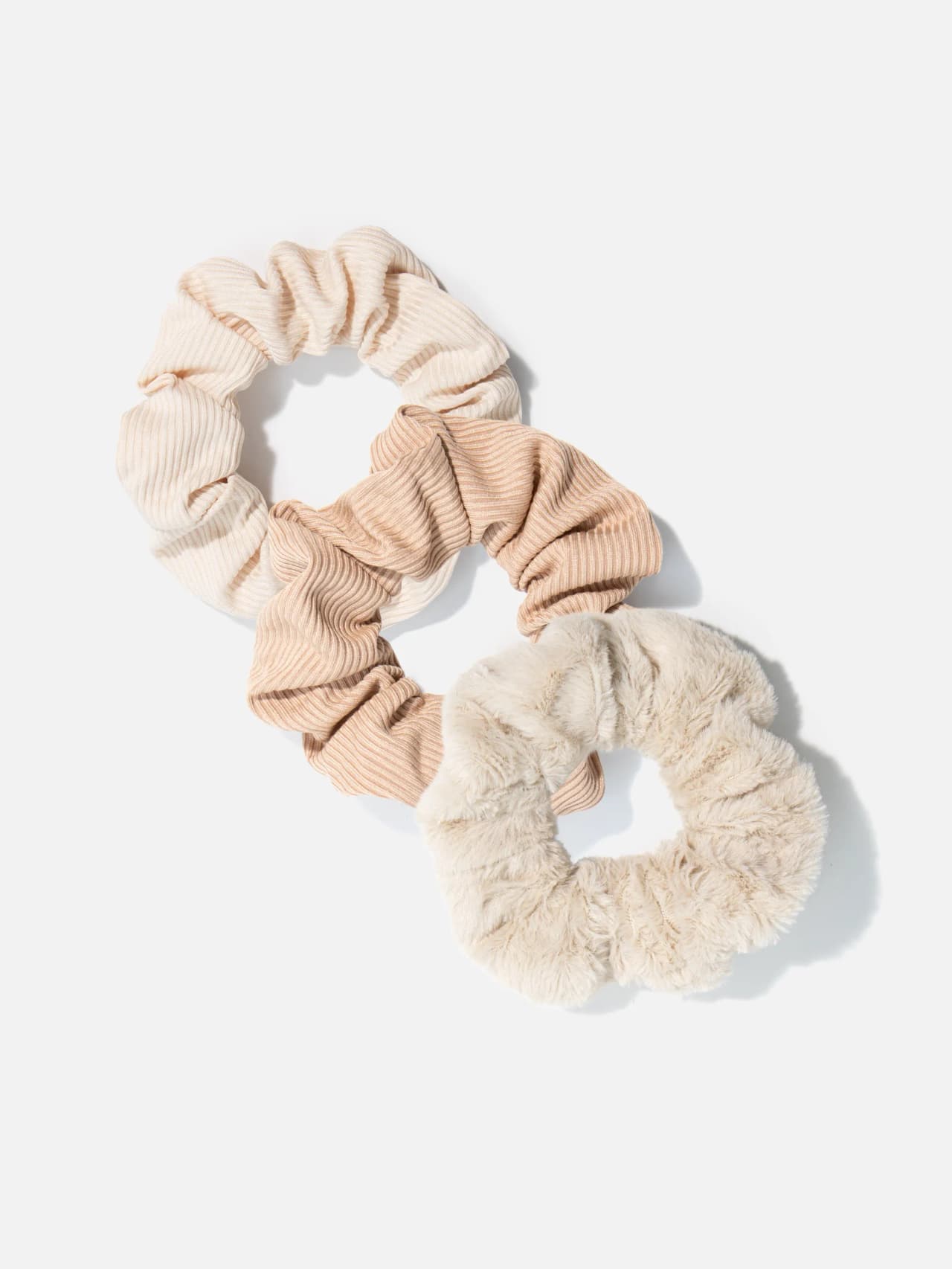 Tre scrunchies i beige och camel på ljus bakgrund